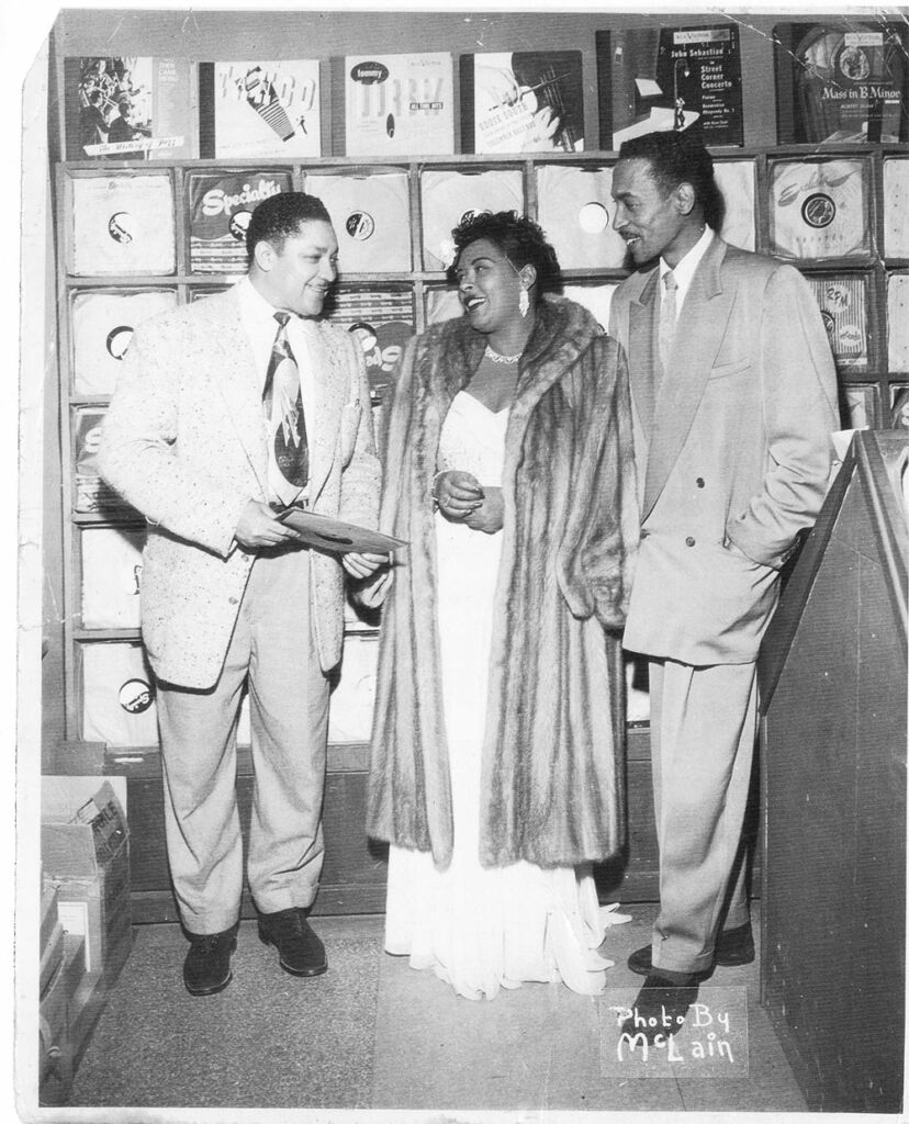 Billie Holiday a centro, com dois homens, um de cada lado