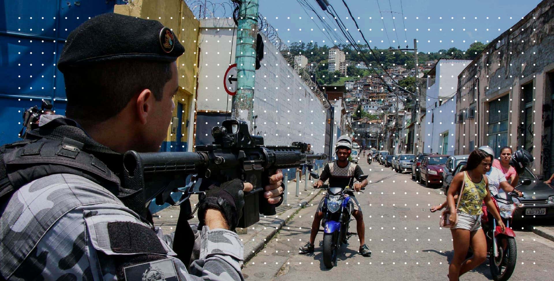 Policial militar apontando fuzil para motociclista na saída de comunidade. (Foto original: Betinho Casas Novas/Estadão Conteúdo)