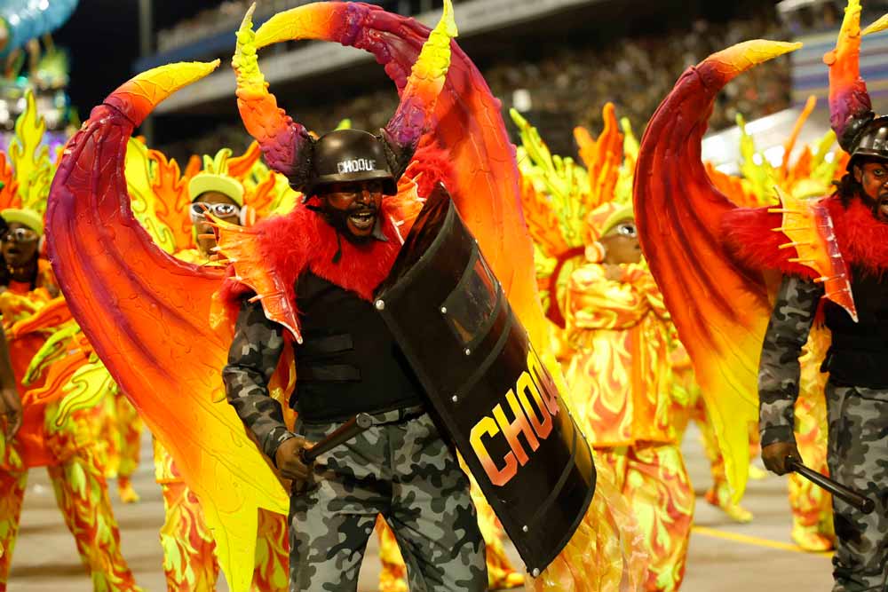 Homem caracterizado com roupas da tropa de choque e asas de demônio.