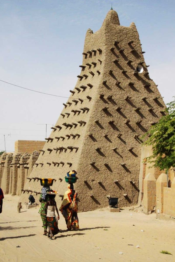 Mulheres caminhando em frente a construção característica do Mali (Imagem: Raul Frare)