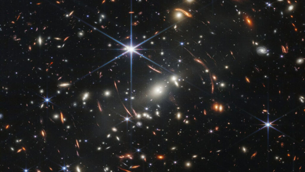 A primeira imagem de campo profundo obtida pelo Telescópio Espacial James Webb mostra galáxias do universo primitivo, ampliadas por um aglomerado galáctico em primeiro plano. (Imagem: Nasa)